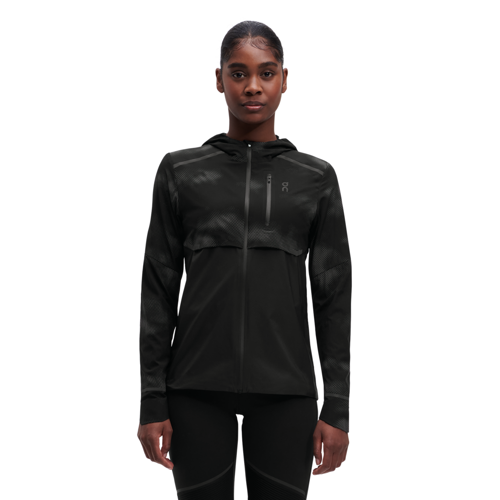 A woman wearing a black weather jacket with reflective elements on the sleeves and chest.