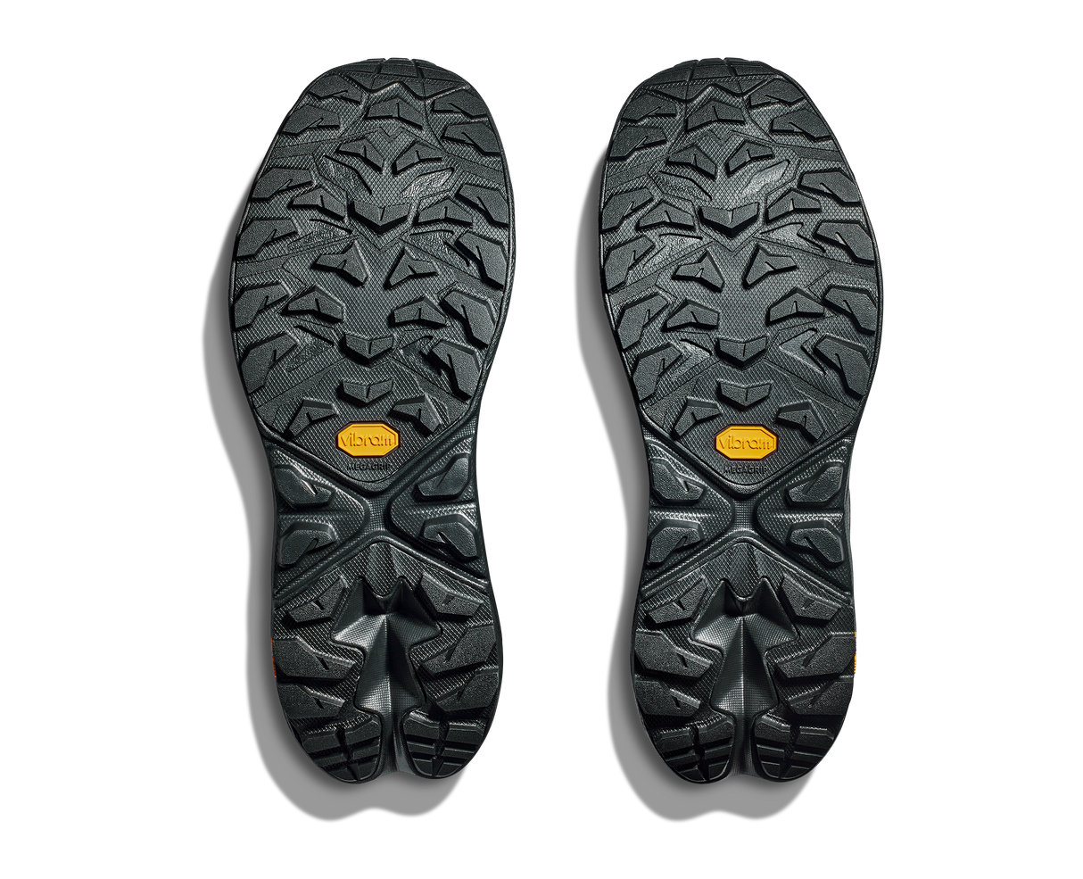 Close-up of black shoe soles with tread pattern and orange Vibram logo on a white background