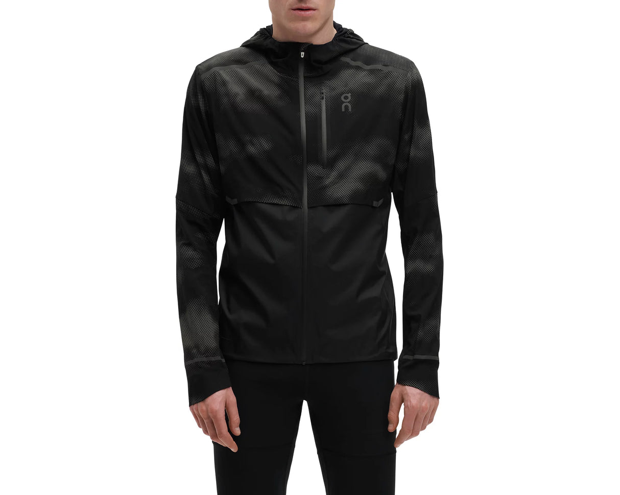 A man wearing a black reflective weather jacket with a hood, zipper, and a logo on the chest.