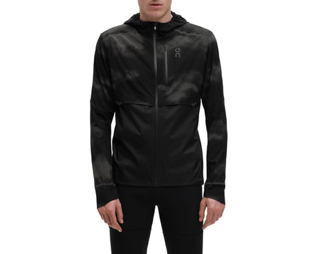 A man wearing a black reflective weather jacket with a hood, zipper, and a logo on the chest.