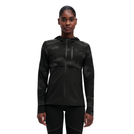 A woman wearing a black weather jacket with reflective elements on the sleeves and chest.