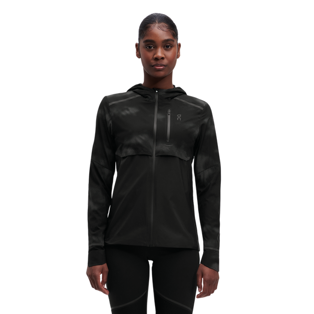 A woman wearing a black weather jacket with reflective elements on the sleeves and chest.
